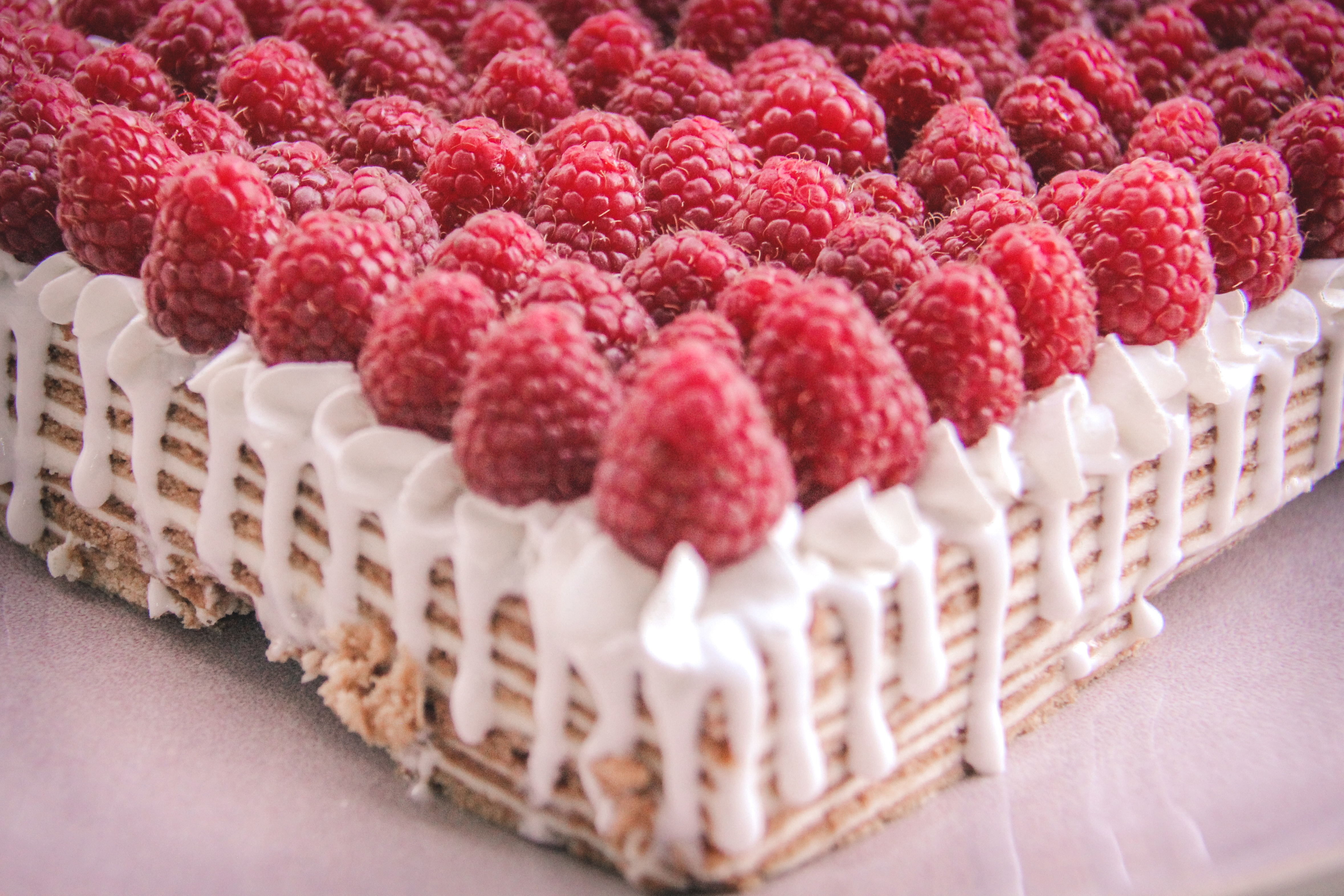 A delicious sheet cake featuring a cascade of raspberries on a bed of creamy white frosting dripping down the edges.