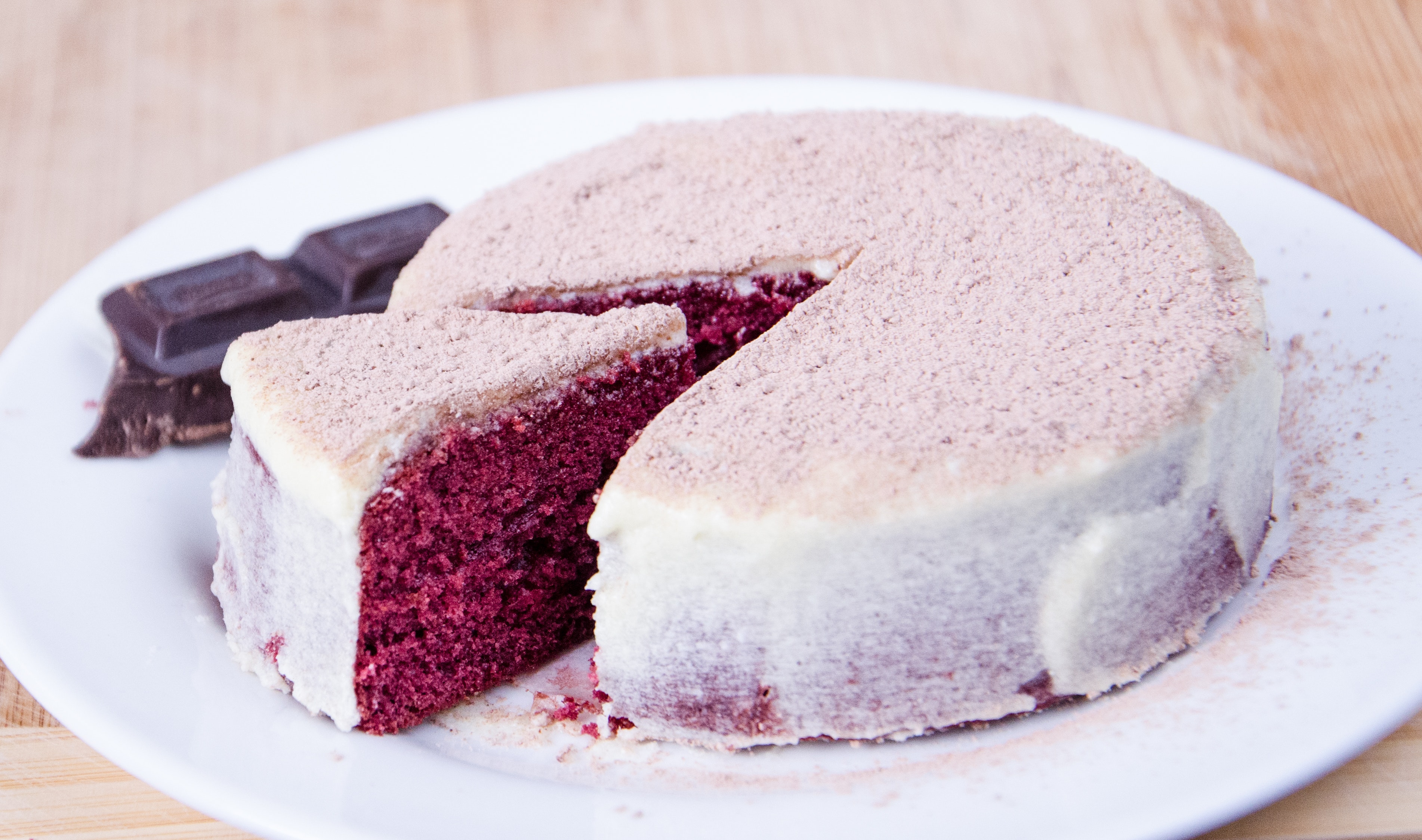 A slice is cut out of a round cake on a white plate. The cake is white with a subtle pink dusting on the top and reveals a deep pink interior.